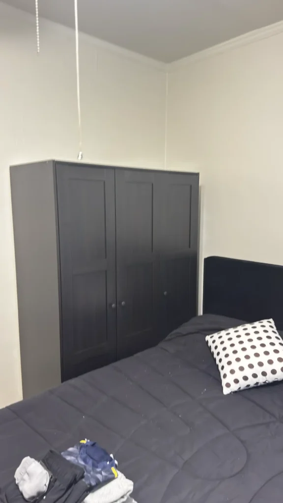 Dark three-door wardrobe assembled beside a bed in Evanston, IL.