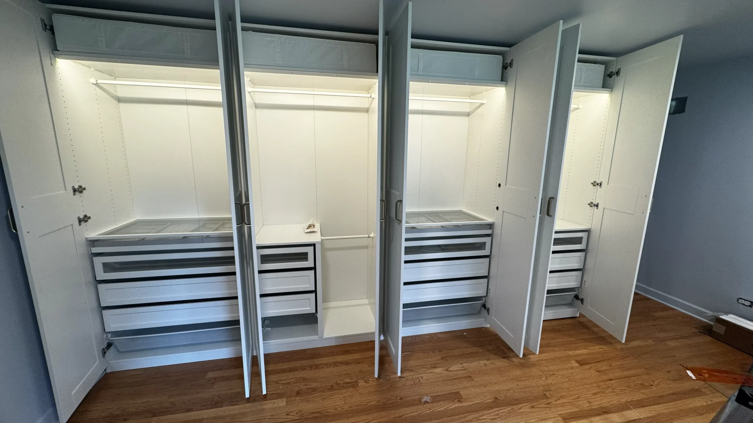 Interior of an open eight-door IKEA PAX wardrobe with lit shelves, hanging rails and pull-out drawers in Palatine, IL