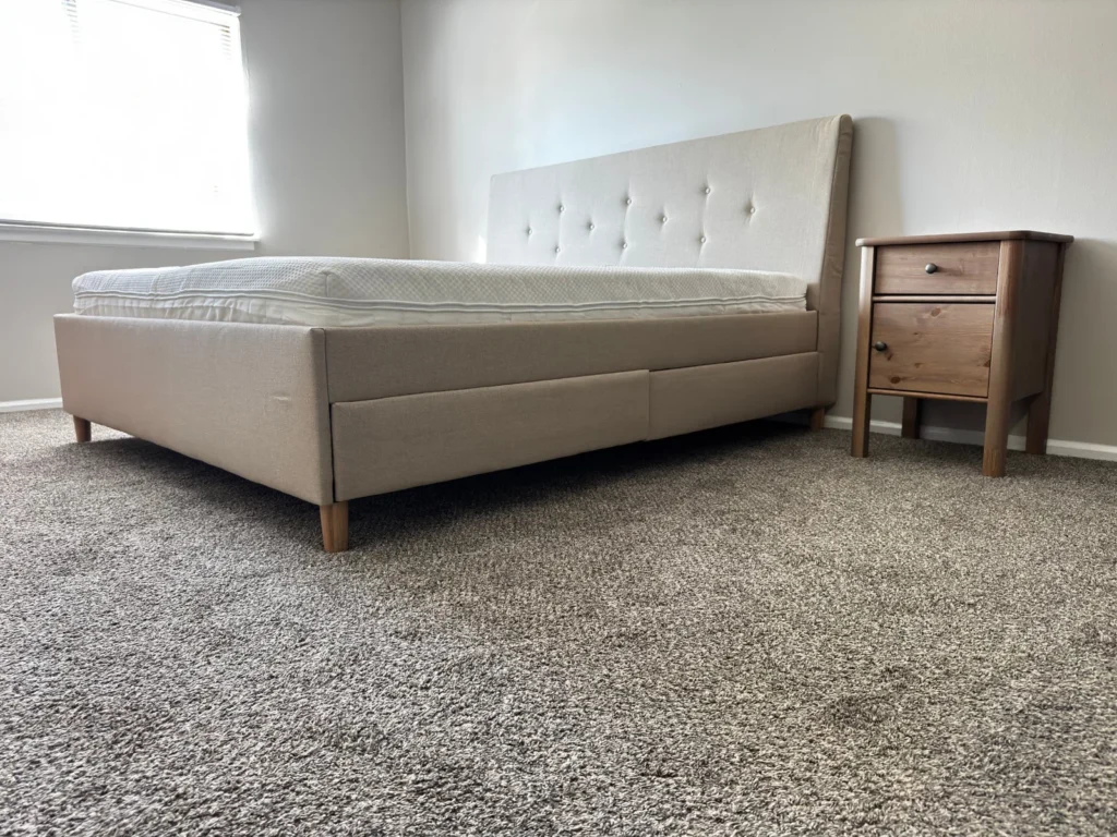 Beige IKEA upholstered storage bed with tufted headboard and pine nightstand assembled in Arlington Heights